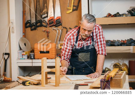 Man in plaid shirt and overalls working on a wooden project in his workshop, drawing on clipboard with pencil. Surrounded by tools and wood, woodworking and DIY craftsmanship, National Carpenters Day Man in plaid shirt and overalls working on a wooden project in his workshop, drawing on clipboard with pencil. Surrounded by tools and wood, woodworking and DIY craftsmanship, National Carpenters Day 120066885
