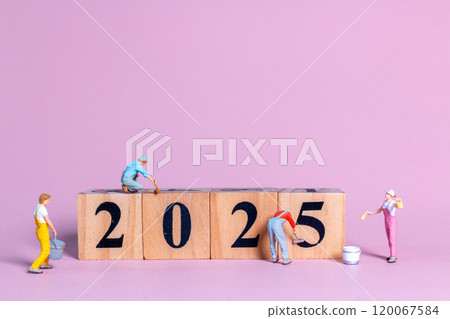 Miniature figures in overalls paint and construct the numbers "2025" on wooden blocks 120067584