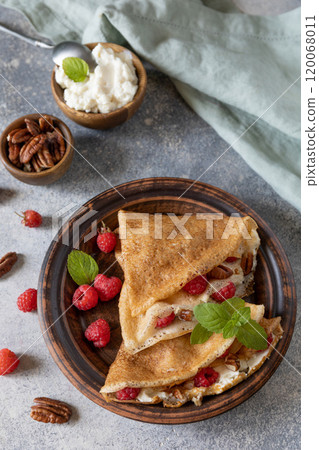Tasty homemade sweet crepes stuffed with raspberries and cream cheese on a gray stone background. Thin pancakes, blini. Sweet dessert. 120068011