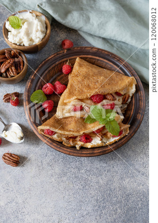 Tasty homemade sweet crepes stuffed with raspberries and cream cheese on a gray stone background. Thin pancakes, blini. Sweet dessert. Copy space. 120068012