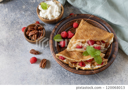 Tasty homemade sweet crepes stuffed with raspberries and cream cheese on a gray stone background. Thin pancakes, blini. Sweet dessert. Copy space. Tasty homemade sweet crepes stuffed with raspberries and cream cheese on a gray stone background. Thin pancakes, blini. Sweet dessert. Copy space. 120068013