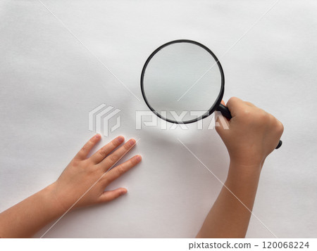 Childs curiosity. Hand holding magnifying glass over white surface Childs curiosity. Hand holding magnifying glass over white surface 120068224