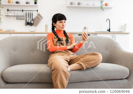 Young woman having video call while sitting on a comfortable sofa 120069046