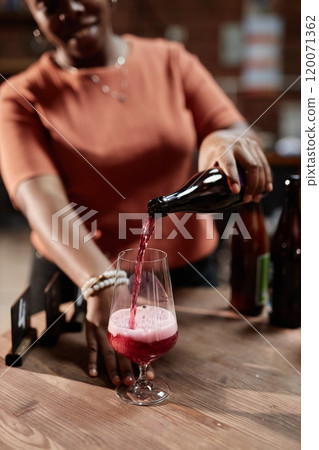 Vertical shot of female African American sommelier pouring craft cider into glass during product sampling in tasting room as part of factory, copy space Vertical shot of female African American sommelier pouring craft cider into glass during product sampling in tasting room as part of factory, copy space 120071362