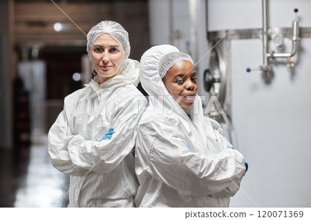 Medium portrait shot of diverse team of two smiling female technicians in coveralls posing for camera with arms crossed in workshop at food factory, copy space Medium portrait shot of diverse team of two smiling female technicians in coveralls posing for camera with arms crossed in workshop at food factory, copy space 120071369