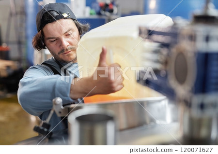 Portrait shot of concentrated male production worker pouring liquid from plastic container into stainless steel tank making craft cider in workshop of factory, copy space 120071627
