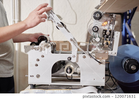 Cropped shot of male factory worker applying labels on bottles using sticker labeling machine at production line at craft cider plant, copy space 120071631