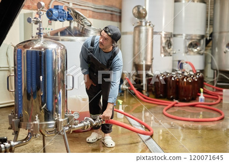 Experienced male cider production worker filling pasteurization machine with juice checking temperature on indicator in workshop at factory, copy space 120071645