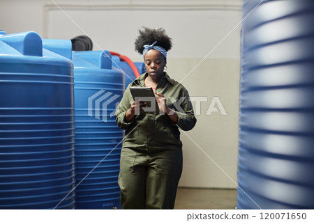 Medium full shot of female African American process technician writing on tablet computer walking along huge plastic barrels while inspecting apple maceration at craft cider factory, copy space 120071650