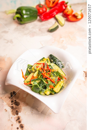 Fresh cucumbers, bell peppers, and herbs on white plate, pink background 120071657