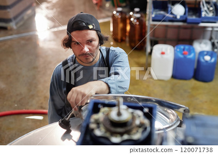 High angle shot of male cider production worker operating pasteurizing machine checking heating process in workshop of factory, copy space High angle shot of male cider production worker operating pasteurizing machine checking heating process in workshop of factory, copy space 120071738