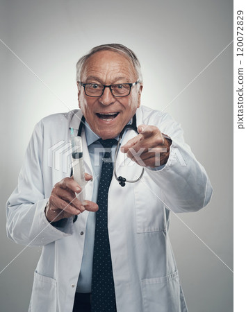 Youll get a lollipop after this injection. Shot of an elderly male doctor holding a syringe for injection in a studio against a grey background. 120072829