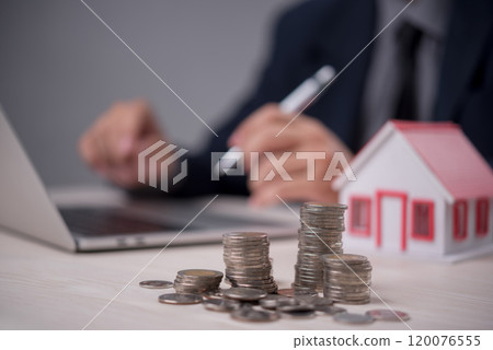 Stacks of coins and a house model with a businessman in the background. Ideal for real estate investment, financial planning, and mortgage services. Wealth management concept. Stacks of coins and a house model with a businessman in the background. Ideal for real estate investment, financial planning, and mortgage services. Wealth management concept. 120076555