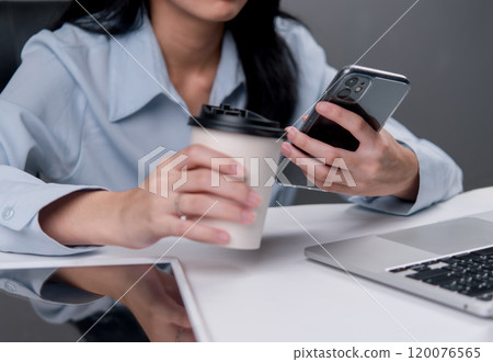 businesswoman holding a coffee cup and checking her smartphone, reflecting a moment of multitasking during a work break. businesswoman holding a coffee cup and checking her smartphone, reflecting a moment of multitasking during a work break. 120076565