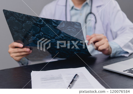 Doctor examining an X-ray image on a desk. Relevant for healthcare, medical diagnostics, radiology, and patient care content. Doctor examining an X-ray image on a desk. Relevant for healthcare, medical diagnostics, radiology, and patient care content. 120076584