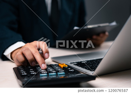 Business professional calculating financial data using a calculator and laptop. Suitable for financial analysis, accounting, audit, or business management content. 120076587