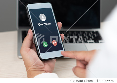 hand holding a smartphone displaying an incoming call from an unknown caller, representing communication, security risks, and mobile technology. 120076670
