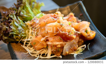 Close-up of marinated salmon poke with fresh lettuce and shredded vegetables in black ceramic dish 120080031