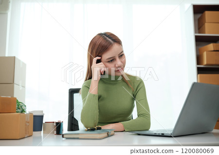 A woman is sitting at a desk with a laptop and a book 120080069