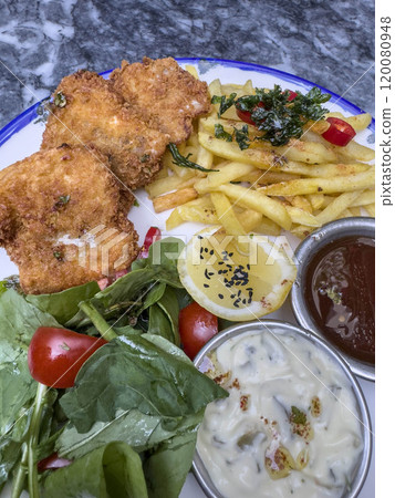 fried fish or chicken served with salad and French fries on plate. 120080948