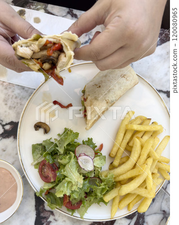 hand holds meat wrap sandwich over plate for lunch or dinner hand holds meat wrap sandwich over plate for lunch or dinner 120080965