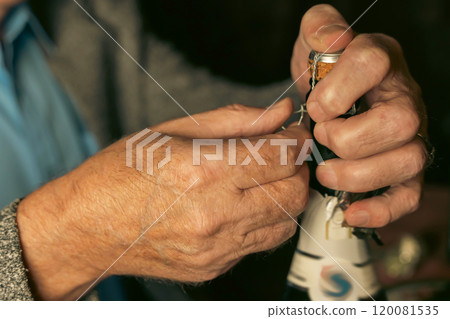 Senior man opening sparkling wine bottle: untwisting wire cage Senior man opening sparkling wine bottle: untwisting wire cage 120081535