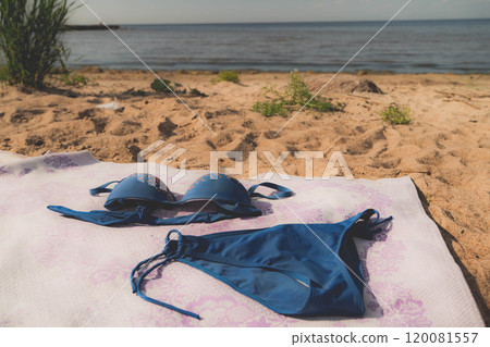 A blue bikini is laid on a sandy beach near the water 120081557
