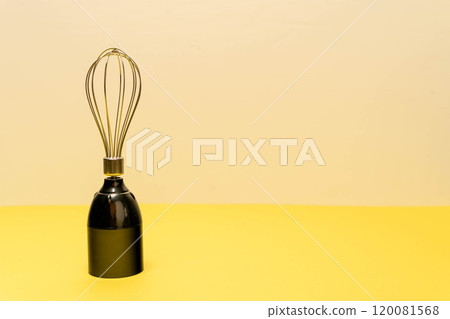A modern whisk is positioned upright on a yellow surface A modern whisk is positioned upright on a yellow surface 120081568