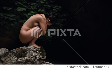 A beautiful naked Asian girl is squatting on a rock in the jungle with her arms wrapped around her legs A beautiful naked Asian girl is squatting on a rock in the jungle with her arms wrapped around her legs 120084587
