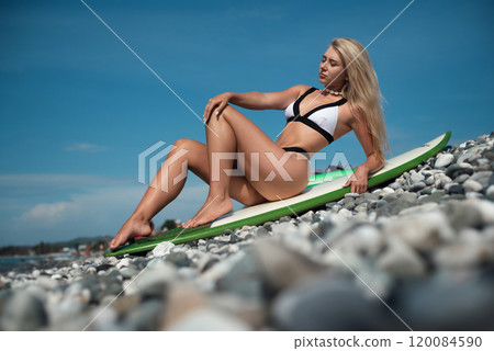 a beautiful girl in a swimsuit with a surfboard on the ocean shore against the background of a beautiful blue sky poses sexually a beautiful girl in a swimsuit with a surfboard on the ocean shore against the background of a beautiful blue sky poses sexually 120084590