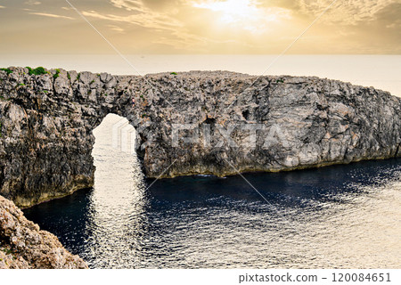 Spectacular sunset at Pont den Gil, Cala Corbetar in Ciutadella, Menorca, Balearic Islands. Peculiar natural formation in the form of an arch Spectacular sunset at Pont den Gil, Cala Corbetar in Ciutadella, Menorca, Balearic Islands. Peculiar natural formation in the form of an arch 120084651