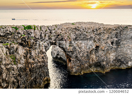 Spectacular sunset at Pont den Gil, Cala Corbetar in Ciutadella, Menorca, Balearic Islands. Peculiar natural formation in the form of an arch Spectacular sunset at Pont den Gil, Cala Corbetar in Ciutadella, Menorca, Balearic Islands. Peculiar natural formation in the form of an arch 120084652