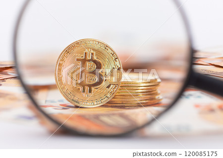 A Stack of Bitcoin Coins Visible Through a Magnifying Glass on the 50-Euro Banknotes 120085175
