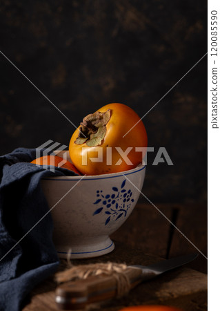 Rustic still life of persimmons in a patterned bowl Rustic still life of persimmons in a patterned bowl 120085590