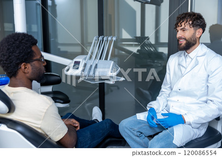 Man dentist in dental office talking with male patient and preparing for treatment 120086554
