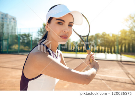Female tennis player in white cap hitting the ball with a racket Female tennis player in white cap hitting the ball with a racket 120086575