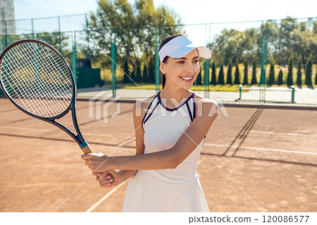 Female tennis player in white cap hitting the ball with a racket Female tennis player in white cap hitting the ball with a racket 120086577