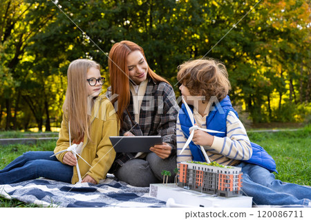 Woman volunteering at camp with children using models of wind turbines and digital tablet 120086711