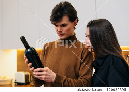 Couple examines wine bottle in a modern kitchen during evening gathering Couple examines wine bottle in a modern kitchen during evening gathering 120086896