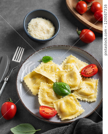Homemade ravioli pasta with cheese, tomatoes and basil in a plate on a dark background Homemade ravioli pasta with cheese, tomatoes and basil in a plate on a dark background 120087316