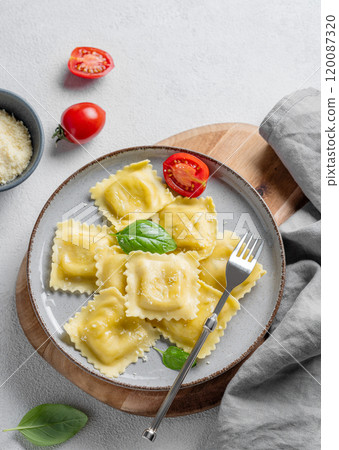 Homemade ravioli pasta with cheese, tomatoes and basil in a plate on a wooden board  120087320