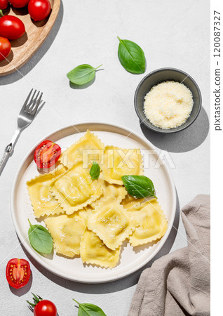 Ravioli pasta with parmesan, tomatoes and basil in a plate on a light  background with shadow 120087327
