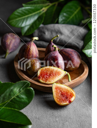 Juicy figs in a wooden plate on a dark background with leaves and a napkin close up. Juicy figs in a wooden plate on a dark background with leaves and a napkin close up. 120087330