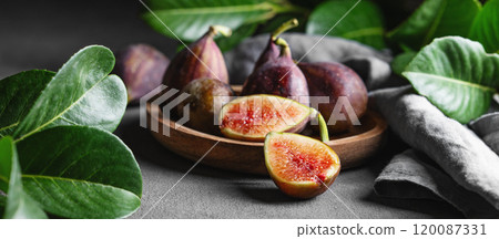 Juicy figs in a wooden plate on a dark background with leaves and a napkin close up. 120087331