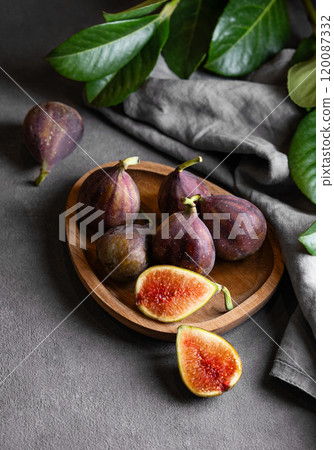 Juicy figs in a wooden plate on a dark background with leaves and a napkin. 120087332