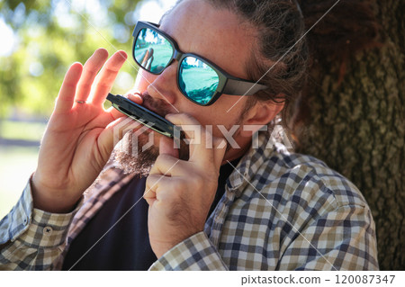 Man with Dreadlocks Ponytail in Sunglasses Playing Harmonica, Mouth Organ 120087347