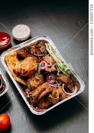 Delicious barbecue assortment in foil trays with tomatoes, sauces, ideal for catering and delivery 120087358