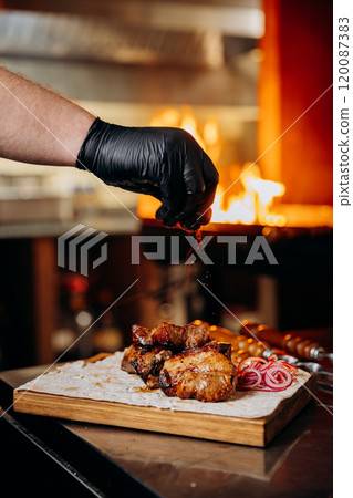 Chefs hand sprinkling seasoning over juicy grilled meat, gourmet barbecue preparation Chefs hand sprinkling seasoning over juicy grilled meat, gourmet barbecue preparation 120087383