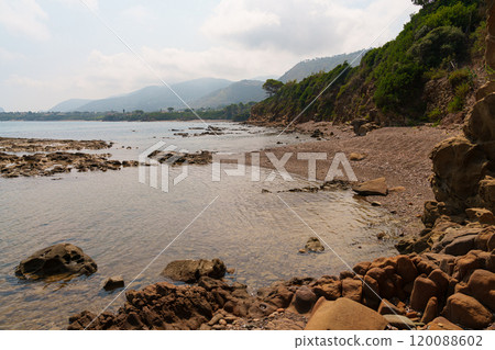 Tranquil Coastal Beach with Rocky Shoreline and Distant Hills 120088602
