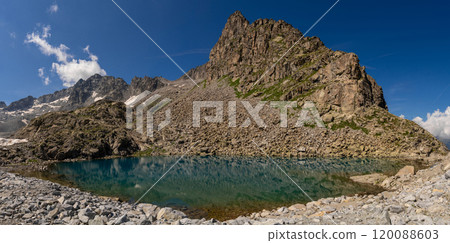Clear mountain lake reflecting rugged cliffs and snow capped peaks in alpine landscape 120088603